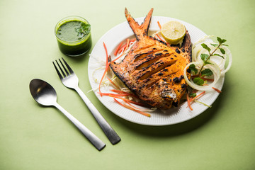 Tandoori Pomfret fish cooked in a clay oven and garnished with lemon , mint, cabbage and carrot salad. Selective focus