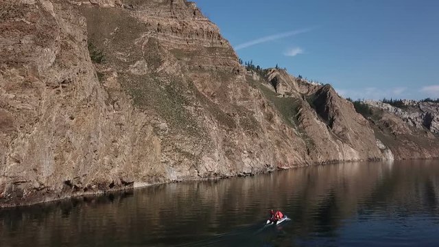 The boat sails along the rocky coast of Lake Baikal. Aerial shooting from the drone.