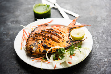 Tandoori Pomfret fish cooked in a clay oven and garnished with lemon , mint, cabbage and carrot salad. Selective focus