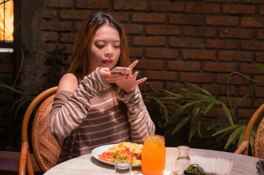 young pretty and happy Asian Korean student girl sitting at sweet coffee shop taking photo of her meal with mobile phone camera in internet social media food blogger concept