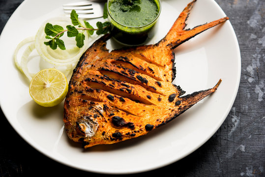 Tandoori Pomfret fish cooked in a clay oven and garnished with lemon , mint, cabbage and carrot salad. Selective focus
