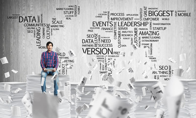 Attractive man sitting on pile of paper documents.