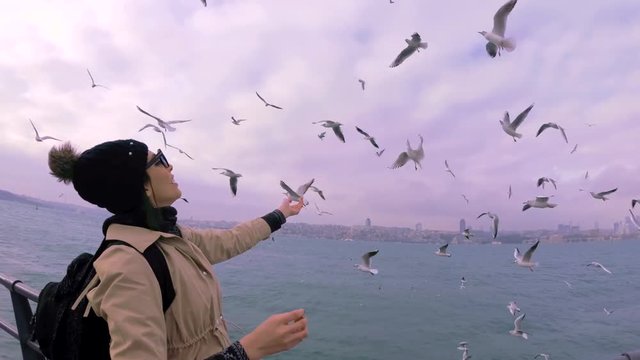 A beautiful woman feeds seagulls with traditional Turkish Street food simit or bagel in English