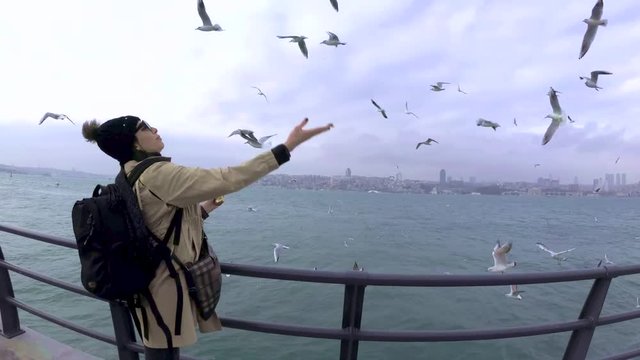 A beautiful woman feeds seagulls with traditional Turkish Street food simit or bagel in English
