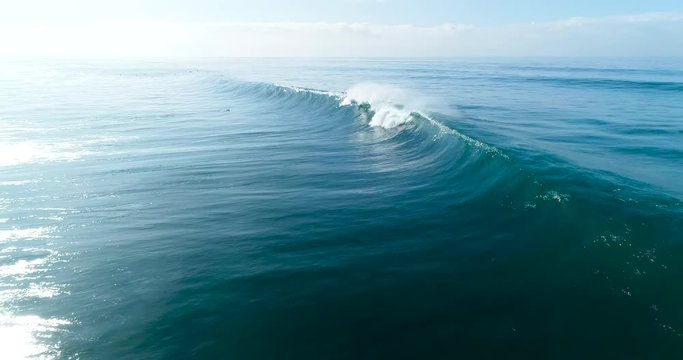 Slow motion aerial view of large blue ocean waves crashing on sunny day 