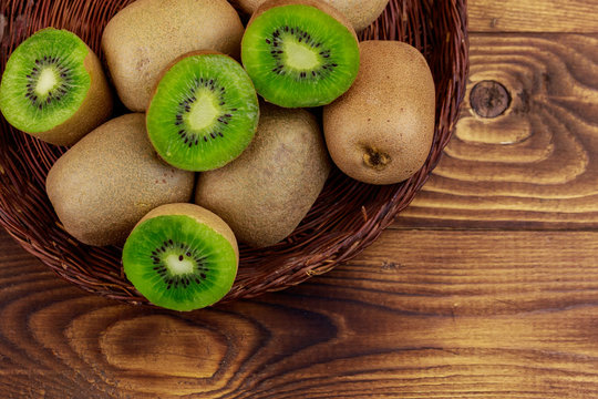 Kiwi fruits in wicker basket on wooden table. Top view