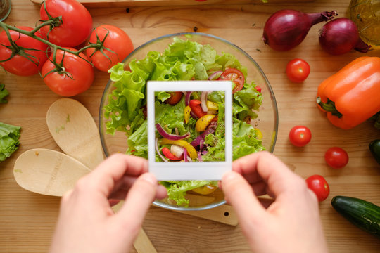 Hands holding photo frame from polaroid over wooden table with fresh vegetables.