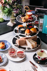 English afternoon tea set including hot tea, pastry, scones, sandwiches and mini pies on marble top...