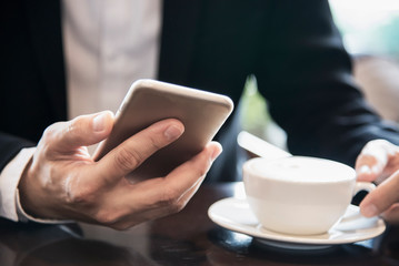 Business man using mobile phone while drinking coffee in coffee shop - modern life style business man in coffee shop concept