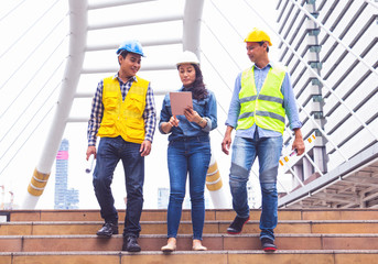 Working engineer. They are walking standing in town and see sky.She play smart phone .They are  mean teamwork  and spirit beside  building background.  Photo concept for engineering  and team work.