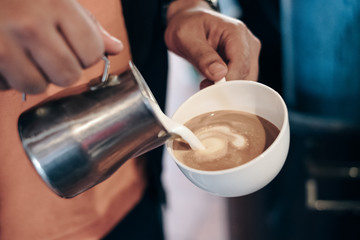 Fototapeta na wymiar Barista pouring milk on coffee cup making heart