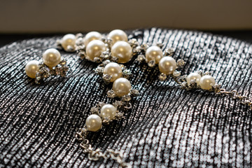 Women's metal jewelry made of pearls. Silver accessory for girls on a silver fabric background, texture. White and milk pearl products with transparent stones and rhinestones.