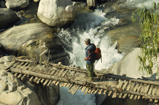 A peasant is walking along the bridge over the river.