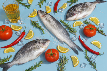 Raw dorada fish with spices, salt, lemon and herbs, rosemary on a ligth-blue background. Top view.