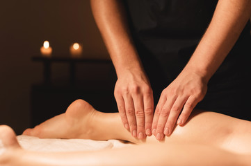Obraz na płótnie Canvas Close-up of male hands doing calf massage of female legs in a dark room with candles in the background. Cosmetology and spa treatments