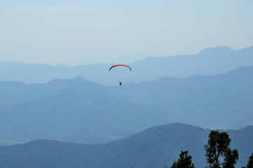 Paragliders are circling in an ascending current above the mountain Sarangkot. Blue sky, multi-colored wings.