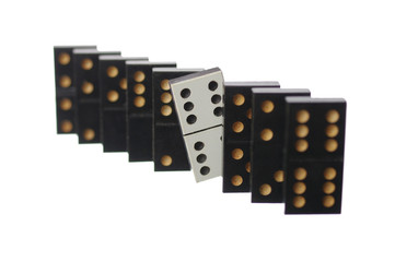 A row of black dominoes and a white one that has fallen out of the row. Isolated on white