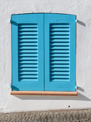 Ventana típica de Mallorca con persianas mallorquinas de color azul claro en una pared blanca