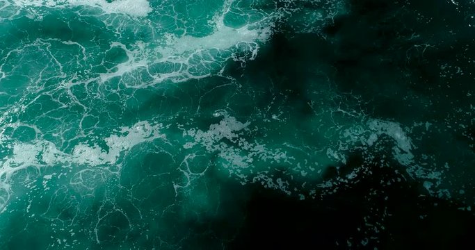 Slow motion top down aerial view of giant ocean waves crashing on sunny day 
