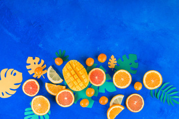 Tropic fruits on a vibrant blue background with copy space. Mango, oranges, kumquat, and other exotic fruits.