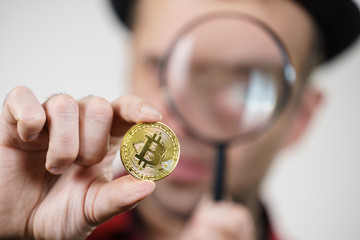 Man looking at bitcoin through magnifying glass