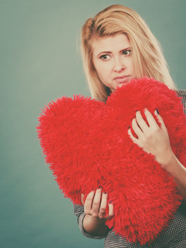 Sad woman holding red pillow in heart shape