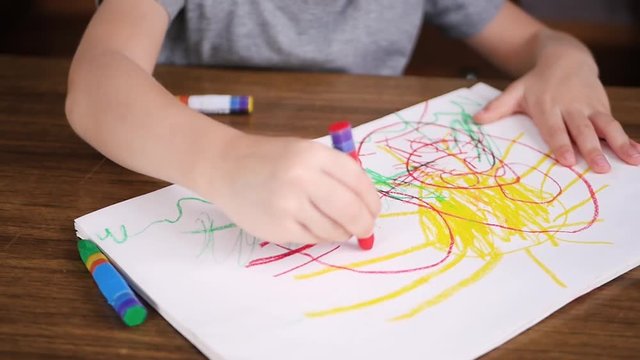 A small child draws a colored pencil, sitting at the table. Hands drawing a child close up.