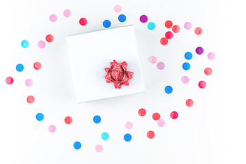 a gift box with red bow flower over multicolored confetti. Present and celebration isolated