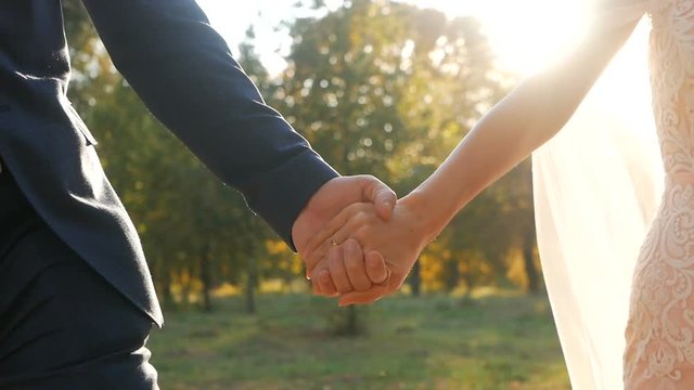 Wedding couple holding hands on sunset background shot in slow motion