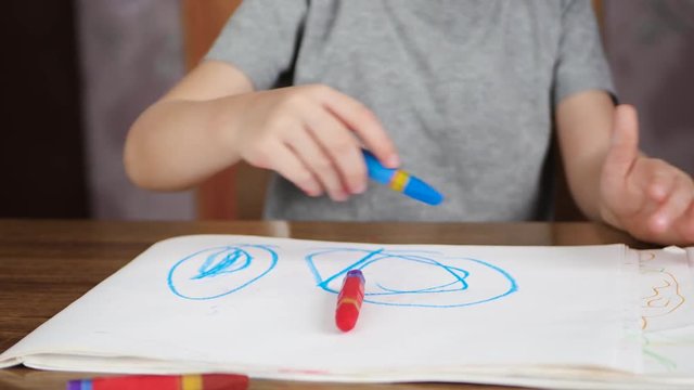 Unknown child draws with bright pencils while sitting at the table. Development and education of children of preschool age.