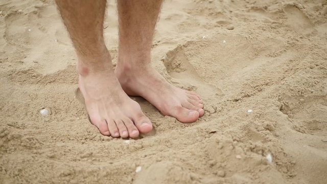 Men's bare feet come in the sand by the sea, leaving a tourist trail.