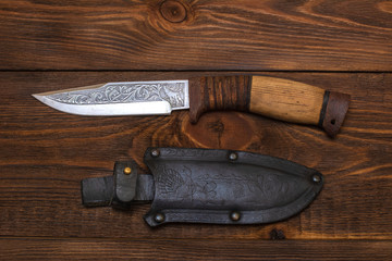 hunting knife wth a wooden handle on dark wooden background. Steel arms weapon