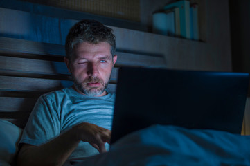 tired and stressed workaholic man working late night exhausted on bed busy with laptop computer feeling sleepy suffering business project deadline stress in funny face