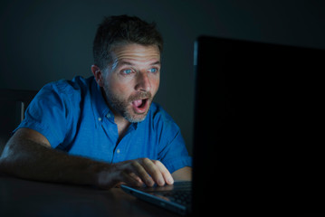 surprised and shocked man at night working with laptop computer in the dark in disbelief and surprise face expression watching something unbelievable in the internet