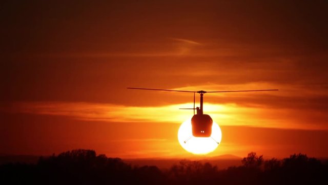 Helicopter on sunset background. Silhouette of a helicopter on a background of bright sun at sunset. Blockbuster shot. Helicopter against the red sky.