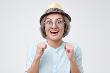 Surprised young woman in hat and glasses with open mouth can not believe her eyes.