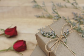 Eco friendly brown paper wrapped gift box present decorated with rose and other flowers on wooden background, valentine ornamental concept