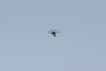 An unmanned aerial vehicle - a quad copter with a camera and a video broadcast flies across the blue sky.