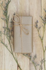 Eco friendly brown paper wrapped gift box present decorated with rose and other flowers on wooden background, valentine ornamental concept