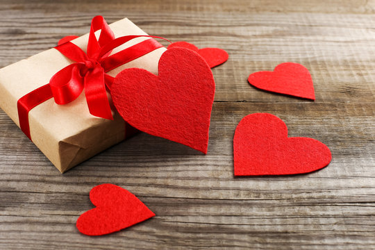 Gift with red ribbon and hearts on wooden background. Women's or Valentine's Day. Place for text, copy space.