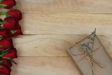 Eco friendly brown paper wrapped gift box present decorated with rose and other flowers on wooden background, valentine ornamental concept