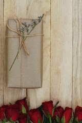 Eco friendly brown paper wrapped gift box present decorated with rose and other flowers on wooden background, valentine ornamental concept