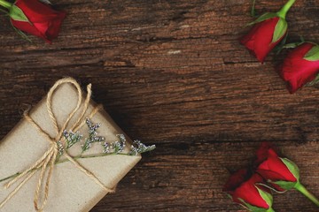 Eco friendly brown paper wrapped gift box present decorated with rose and other flowers on wooden background, valentine ornamental concept
