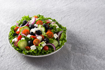 Fresh Greek salad in Plate with black olive,tomato,feta cheese, cucumber and onion on gray background. Copyspace
