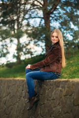 Obraz premium Attrective young girl sits by the embankment. Blond hair and brown jacket. Spring