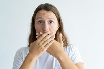 Worried woman covering mouth with hands. Pretty lady looking at camera. Embarrassment concept. Isolated front view on white background.