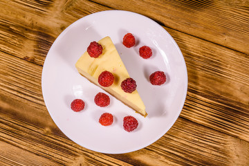White plate with cheesecake New York and raspberries on wooden table. Top view