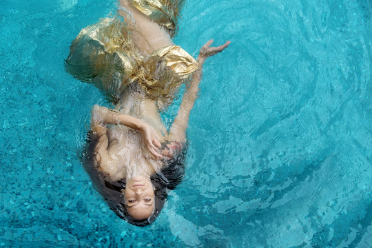 Draufsicht einer sch&ouml;nen jungen sexy Frau in goldenem Kleid, Abendkleid, Tuch schwebt schwerelos elegant schwimmend im Wasser im Pool