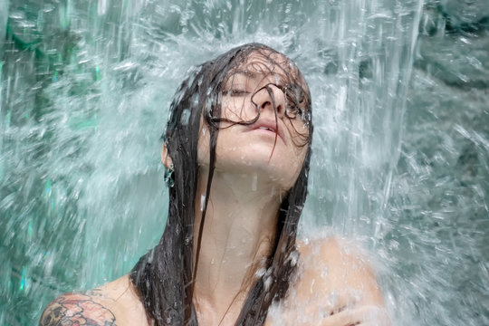Portrait einer schönen jungen sexy Frau unter dem spritzenden Wasser des Wasserfalls  im Wellness Pool
