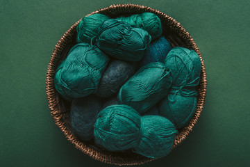 top view of green and blue yarn clews in wicker basket on green backdrop